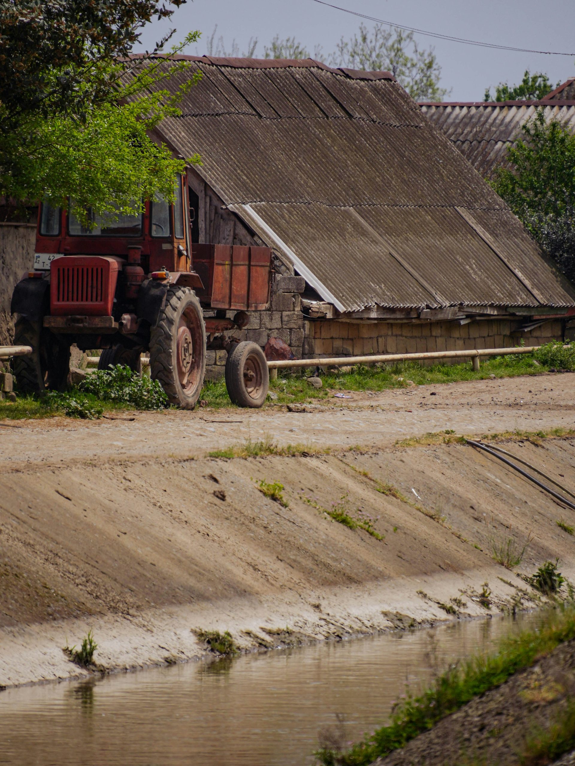 An old red tractor sits next to a canal.
