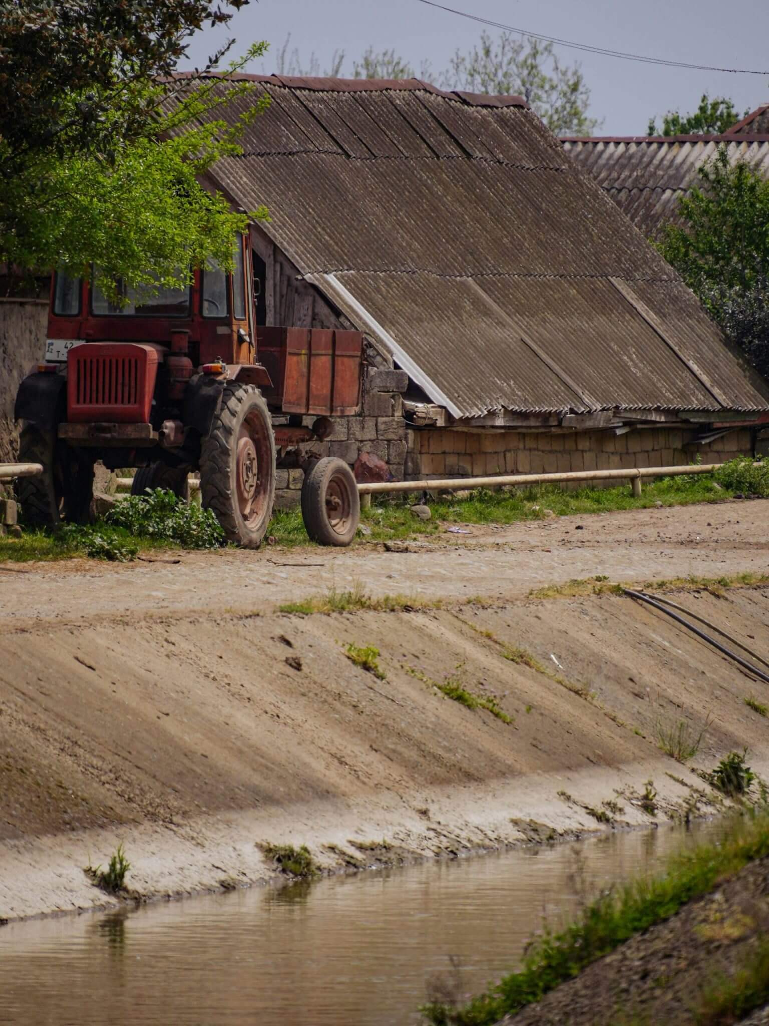 An old red tractor sits next to a canal.